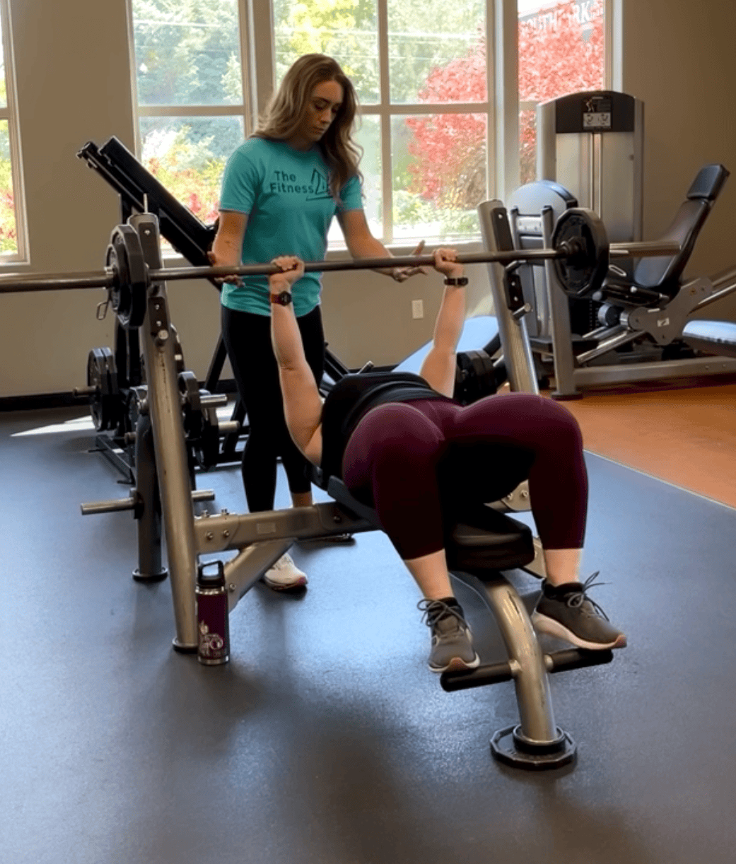 Female personal trainer Allie smith spotting a client while lifting during her in person session